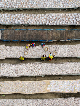 Cox's Bazar, Bangladesh - 11 March 2026: Aerial view of workers spreading and drying small fish on long bamboo mats in a traditional processing yard.