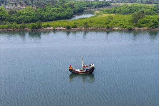 Cox's Bazar, Bangladesh - 11 March 2026: Aerial view of a traditional wooden fishing boat floating on the calm blue waters of a river near lush green mangroves.