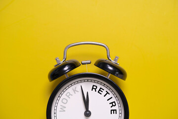 Naklejka premium Work retirement concept with alarm clock on yellow background, symbolizing retirement planning, career transition, pension savings, work life balance and future financial freedom preparation