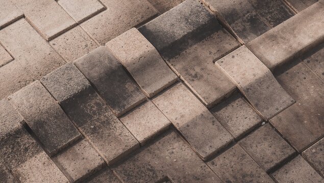 A detailed high angle shot of interlocking rectangular stone pavers showcasing a textured surface and gradient earth tones in a geometric pattern
