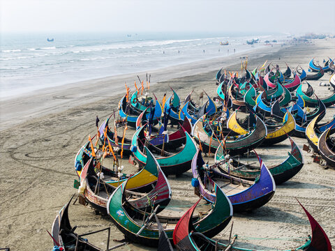 Cox's Bazar, Bangladesh - 10 March 2026: Aerial view of colorful crescent-shaped moon boats parked on the sandy shore of the beach under a hazy sky.