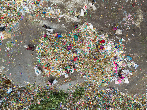 Aminbazar, Bangladesh - 26 January 2025: Aerial view of waste pickers sorting through piles of colorful plastic and organic trash at the Aminbazar landfill with white sacks scattered on the ground.