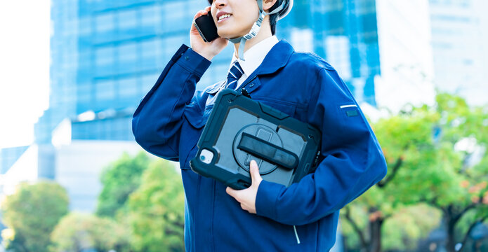 タブレットを持ち電話をする作業着を着た男性