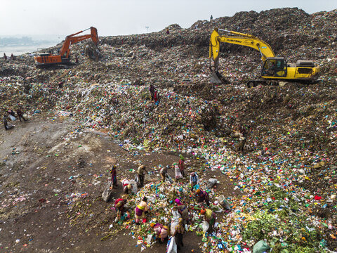 Aminbazar, Bangladesh - 26 January 2025: Aerial view of Aminbazar landfill with excavators and waste pickers sorting through garbage under a hazy sky.