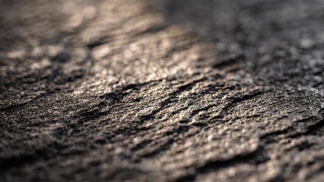 Close-up textured surface of weathered grey stone with dramatic light and shadow creating a rugged abstract background