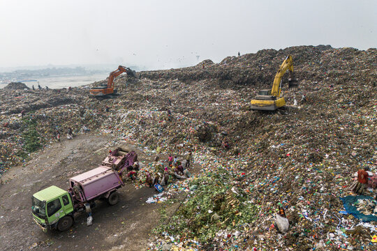 Aminbazar, Bangladesh - 26 January 2025: Aerial view of the Aminbazar landfill with excavators and people scavenging through massive piles of waste under a hazy sky.