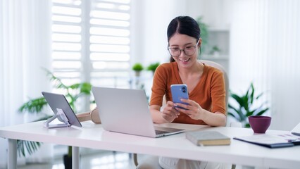Asian businesswoman using smartphone laptop tablet hybrid work from home office desk workspace...