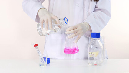 Fototapeta premium Scientist Pouring Clear Liquid into Flask with Pink Phenolphthalein Solution