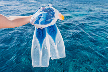 A person holds a full face snorkel mask and pair of flippers over the beautiful turquoise blue ocean water Snorkeling is a popular activity for tourists and vacationers in tropical © Ilja