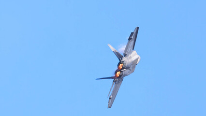 Stealth fighter jet climbing with glowing afterburners against clear blue sky © blueringmedia