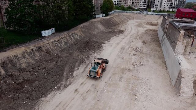 Wheel loader driving on dirt track in large excavation pit in an urban area. Aerial drone