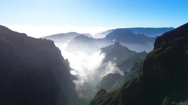 Aerial footage captures a thick sea of clouds filling a deep mountain ravine on Madeira Island while rugged peaks rise above, revealing sunlit slopes and dramatic contrasts between shadowed valleys an
