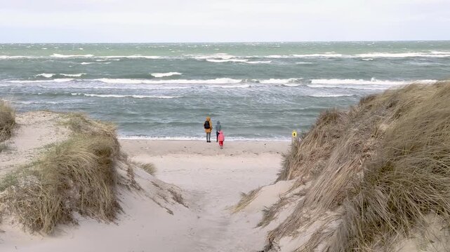 A woman and two children are walking on the beach near the Baltic Sea resort of Ahrenshoop in stormy weather, while the waves of the Baltic Sea roll toward the shore.