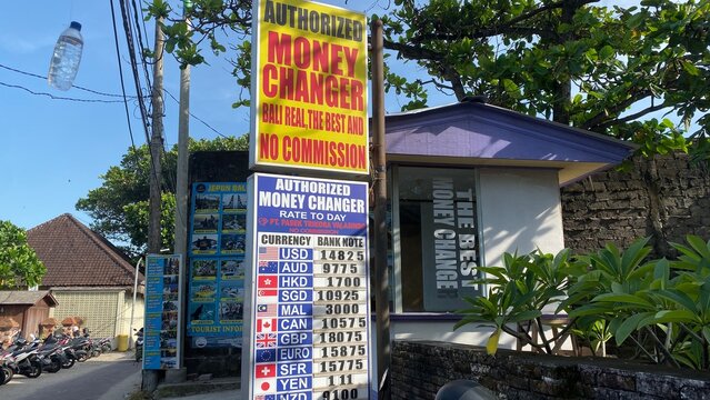 Authorized money changer street signage showing foreign currency exchange rates and tourist information in Kuta tourist district - Bali, Indonesia, March 23, 2023