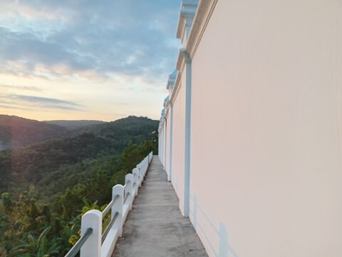 A narrow, paved path runs alongside a tall, white wall with decorative blue trim on a hillside