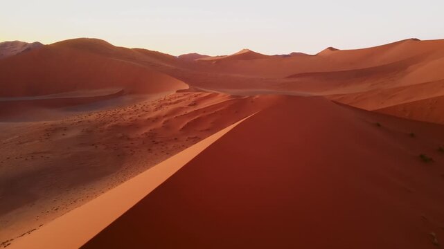 Drone footage captures the vast Namib Desert with towering red sand dunes glowing under the low setting sun, revealing breathtaking panoramic views of shifting patterns and timeless desert beauty.