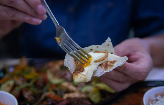 manejo de alimentos, manos femeninas tomando una rebanada de queso fresco sobre tortilla de harina con un  tenedor, al fondo platillo con FAJITAS