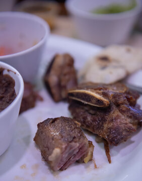 Costillas de res fritas sobre plato blanco de ceramica con frijoles negros refritos, como parte de una comida tipica de Mexico. Vertical
