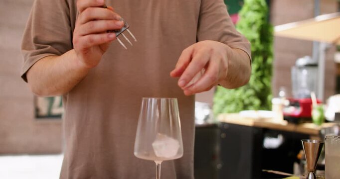 Crushing ice. Bartender occupation. Unrecognizable professional barman male hands cube with tool in transparent glass for making beverage in bar.