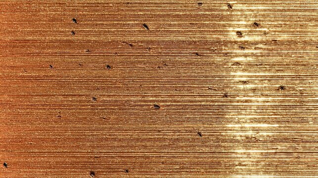 the image presents a brushed copper texture, featuring distinct parallel striations across its surface. bright, elongated light reflections emanate from the bottom right of the frame, arcing upwards a