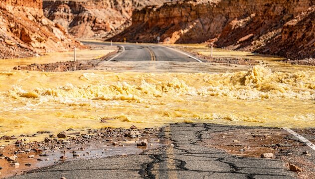 Yellow flash flood water flowing across a cracked desert road for environmental hazard reporting, disaster management news and nature documentary background