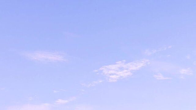 Gentle movement of soft clouds across pale blue sky.