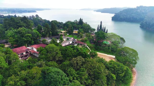 Vista a&eacute;rea de &aacute;rea residencial &agrave; beira de lago cercada por natureza e vegeta&ccedil;&atilde;o densa.