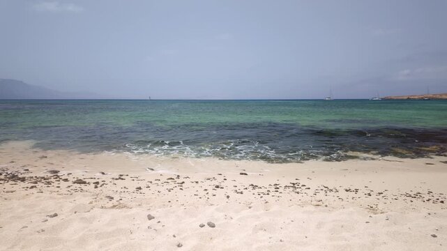 Gentle turquoise waves washing over a sandy beach in La Graciosa