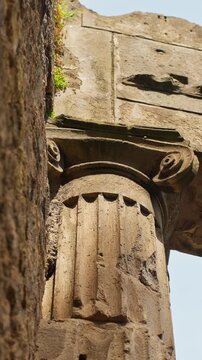 Vertical close-up of a weathered Ionic column in Pompeii, showing carved volutes, fluted stonework, and preserved Roman architectural detail inside the ancient ruins.