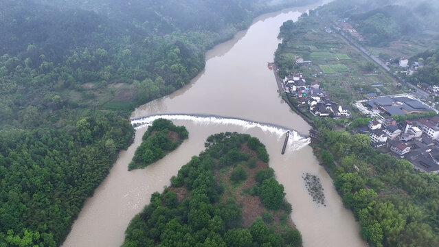 Aerial view of a river with a weir dam flanked by villages and lush green forests