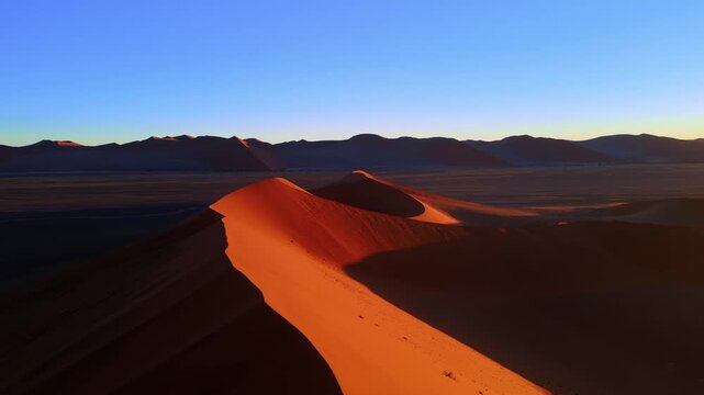Drone footage captures the vast Namib Desert with towering red sand dunes glowing under the low setting sun, revealing breathtaking panoramic views of shifting patterns and timeless desert beauty.