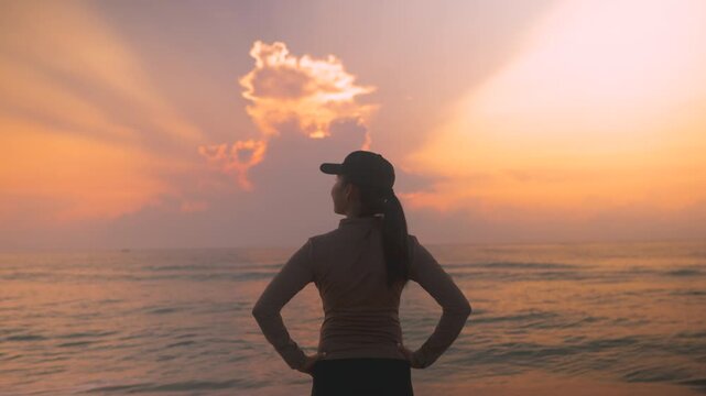 Back view of female traveler enjoying peaceful sunrise over the sea with open arms. Cinematic beach lifestyle footage with warm light, freedom, self care and uplifting travel wellness atmosphere.