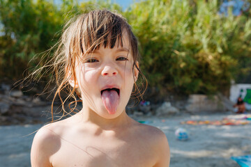 Fototapeta premium Playful Young Girl Sticking Out Tongue at Beach During Summer Vacation