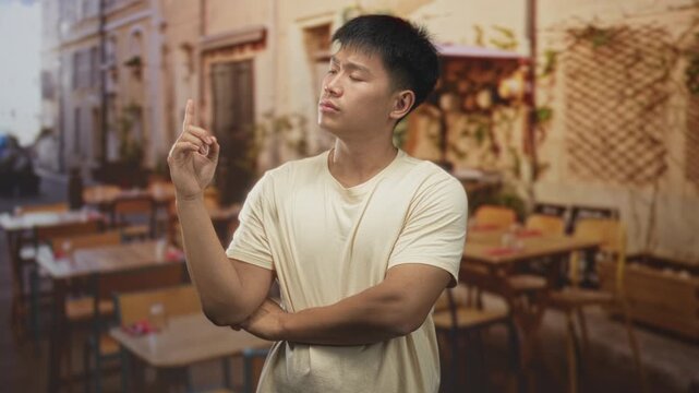 Man points finger upward with crossed arms in a street cafe building dining area with wooden tables and chairs; thoughtful reflection.