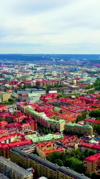 Vertical video. Gothenburg, Sweden. Aerial panorama over the historic city center with red-tiled rooftops, the winding Gota Alv river, and distant harbor cranes under an overcast summer sky.. Drone f