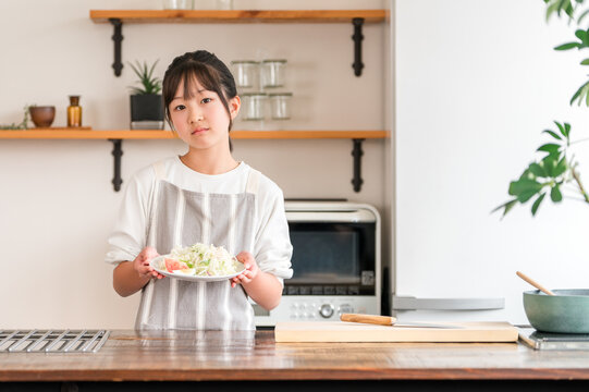 A child/girl/kid holding vegetables in the kitchen (distressed/dislikes vegetables/picky eaters)