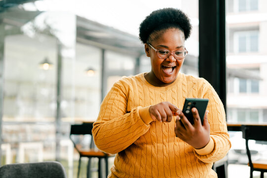 Happy black woman celebrating success using smartphone