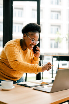Black young woman making phone call working with laptop
