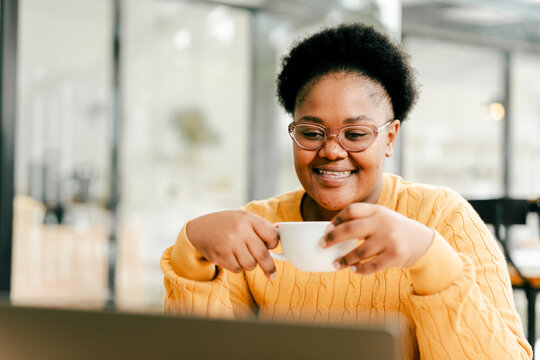 Young black woman smiling holding coffee cup using laptop