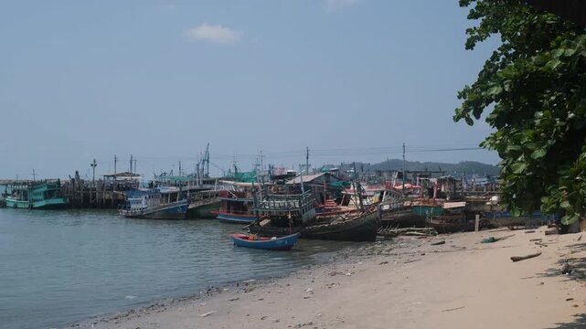 Pile of old abandoned and broken fishing boats and ferries discarded near the pier with calm sea and coastline in the background