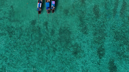 Top-down aerial view of three traditional longtail boats in turquoise water © blueringmedia