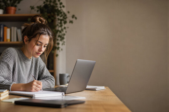 Young woman studying and writing notes at home as online learning concept

