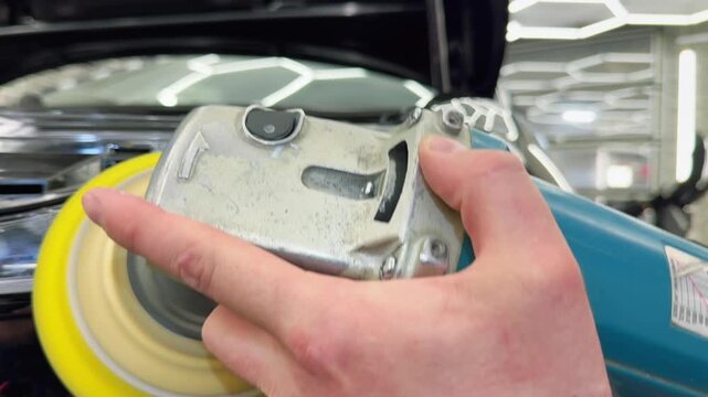 A car service worker polishes the car body with a polishing machine. Detailing and polishing of the car. Car detailing - hands with an orbital polishing machine in an auto repair shop.Selective focus.