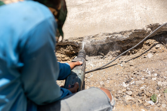 A construction worker using power drill to bore into a concrete curb.