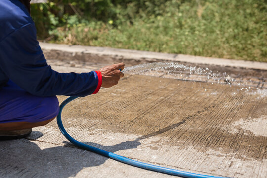 Construction worker wash down a newly laid concrete surface with a water hose.