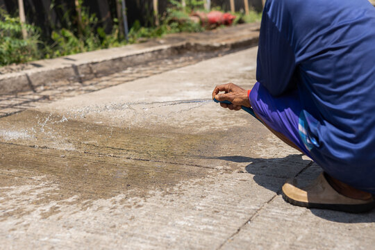 Construction worker wash down a newly laid concrete surface with a water hose.