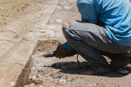 A construction worker using power drill to bore into a concrete curb.