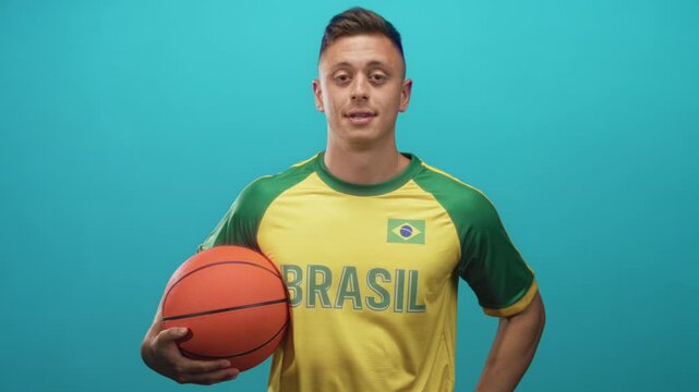 Man holding basketball with right hand, wearing yellow and green brasil jersey with flag patch in studio; team pride confidence.