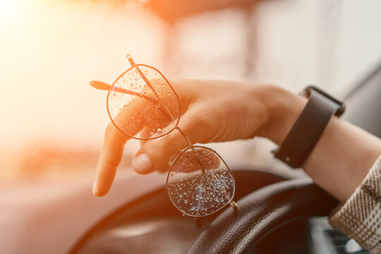 Eyeglasses raindrops car hand holding wet glasses over a steering wheel during a rainy golden hour commute