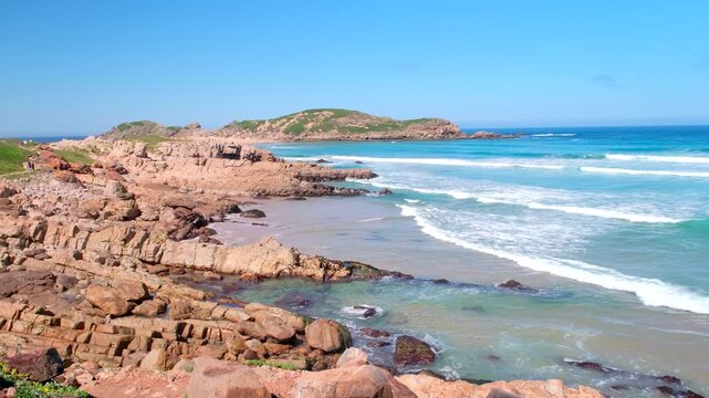 View along rocky shoreline as waves roll in toward The Island, Robberg peninsula